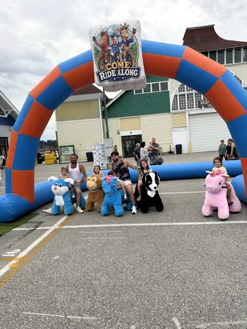 A family posing with plush animal scooters under the Come Ride Along inflatable arch